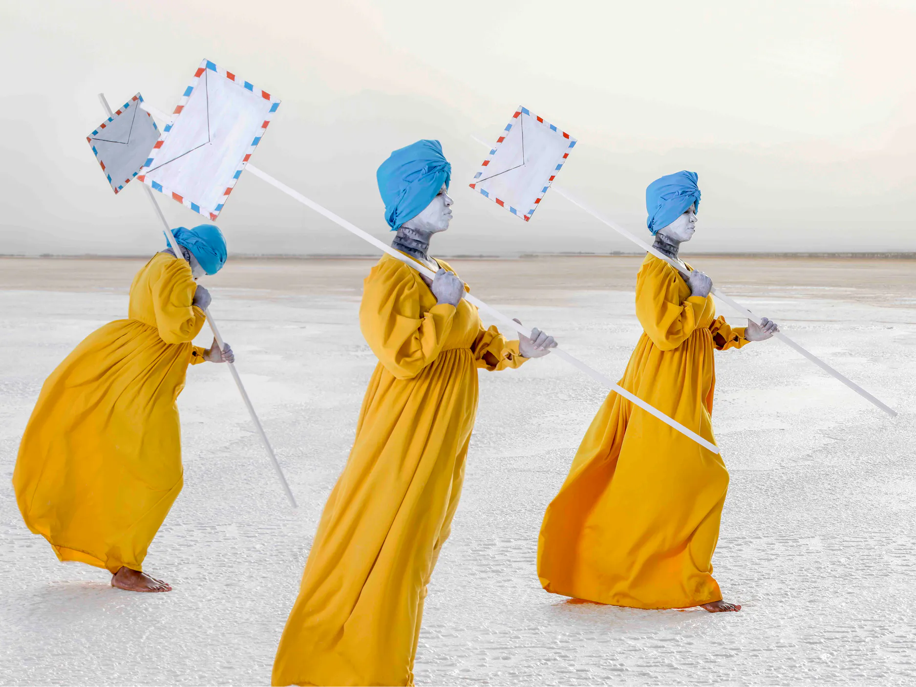 Tri osebe v rumenih haljah in modrih rutah v rokah držijo palice s pisemskimi ovojnicami